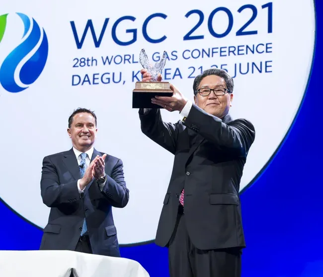 World Gas Conference award recipient lifting a trophy as another participant applauds