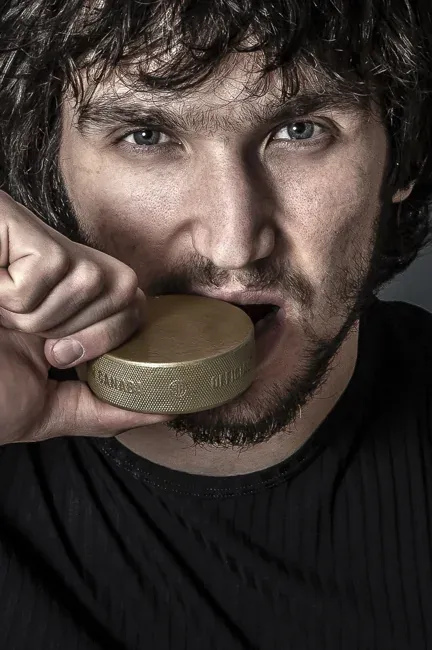Portrait of Alex Ovechkin holding a gold hockey medal near his face