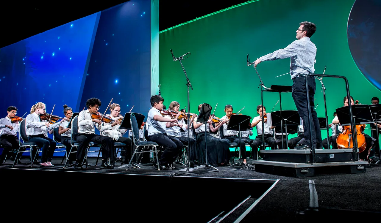 Conductor leading musicians on a blue and green conference stage