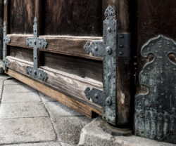 Close-up of ornate metal hinges on a large wooden door, set against a stone-paved ground. The doors dark wood and intricate metalwork evoke a rustic, historical feel—a picturesque backdrop perfect for corporate photography services aiming to capture timeless elegance.