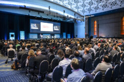 A corporate photo of attendees watching a presentation at a conference.